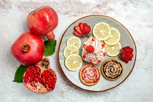 Frischer Granatapfel der Draufsicht mit Kuchen- und Zitronenscheiben auf weißem Raum