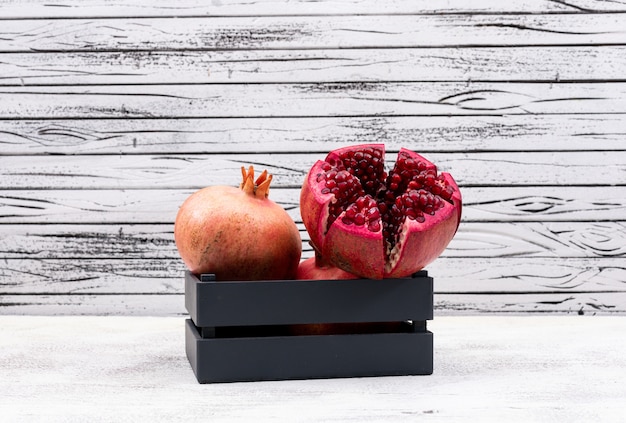 frischer Granatapfel im schwarzen Korb auf weißem Holztisch
