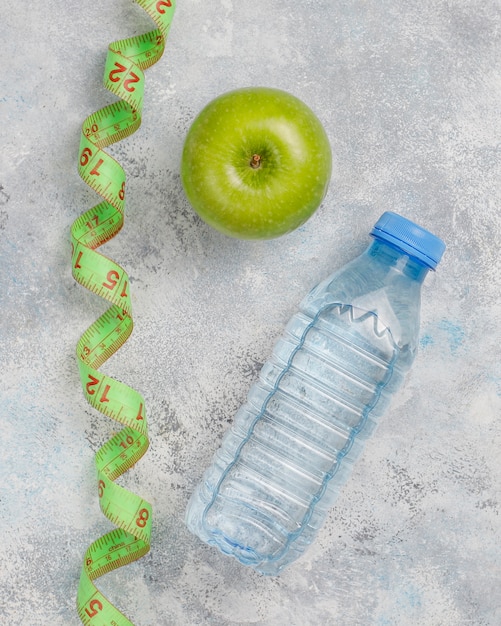 Frischer grüner Apfel, Maßband und Flasche Süßwasser auf grauem Beton