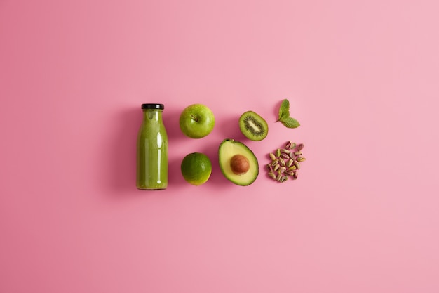 Frischer organischer grüner Smoothie und Zutaten Apfelkalk, Hälfte Avocado, Pistazie und Minzblatt auf rosa Hintergrund. Vegetarisches alkoholfreies Nährgetränk. Natürliches Entgiftungsfutter. Diätkonzept