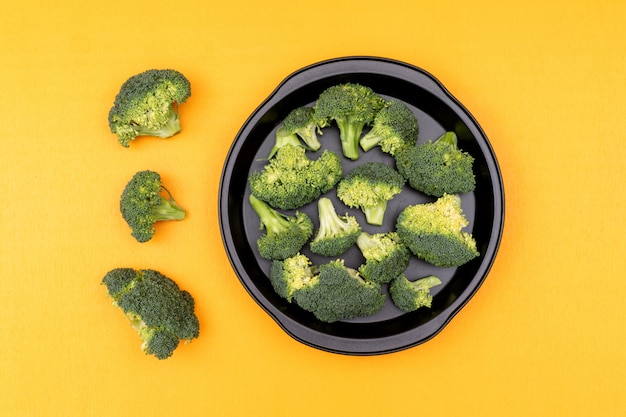 Kostenloses Foto frischer roher grüner brokkoli in einer bratpfanne auf gelber oberfläche