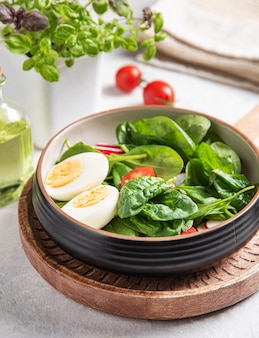 Frischer salat aus grünen spinatblättern, tomaten, gekochtem ei, rotem rettich und olivenöl mit leinsamen. das konzept der gesunden, diätetischen und veganen ernährung hautnah.