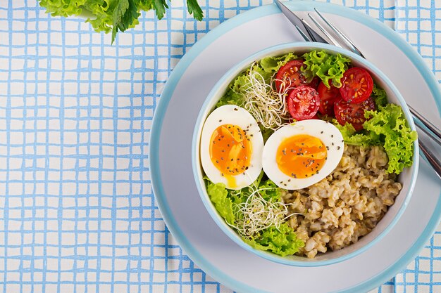 Frischer Salat. Frühstücksschüssel mit Haferflocken, Tomaten, Salat, Microgreens und gekochtem Ei. Gesundes Essen. Vegetarische Buddha-Schüssel. Draufsicht, flach liegen