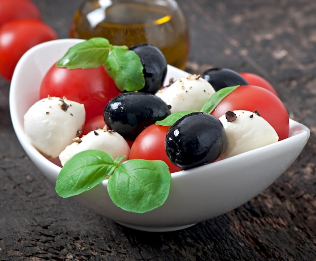 Kostenloses Foto frischer salat mit kirschtomaten, basilikum, mozzarella und schwarzen oliven.