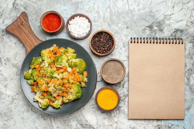 Frischer und gesunder Gemüsesalat auf hölzernem Schneidebrett und Notizbuch auf weißem Tisch