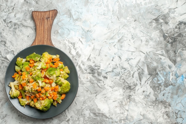 Frischer und gesunder Gemüsesalat auf Holzschneidebrett auf der linken Seite des weißen Tisches