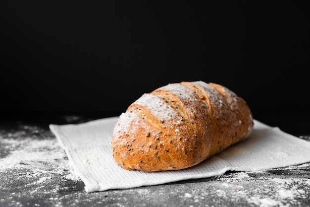 Frisches Brot der Vorderansicht auf schwarzem Hintergrund und Stoff mit Mehl