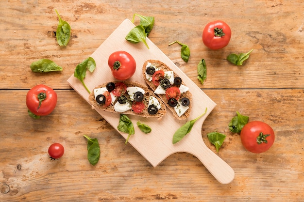 Frisches bruschetta auf dem hölzernen schneidebrett umgeben mit spinat und tomate