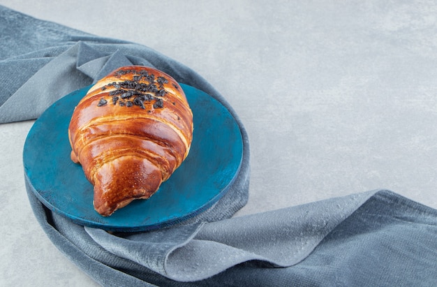 Frisches Croissant verziert mit Tropfenschokolade auf blauem Brett.