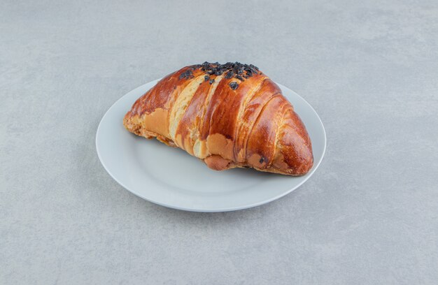 Frisches Croissant verziert mit Tropfenschokolade auf weißem Teller.