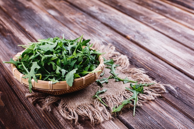 Frisches Essen, gesundes Leben. Grüner Arugula diente in der Schüssel auf rustikalem Hintergrund