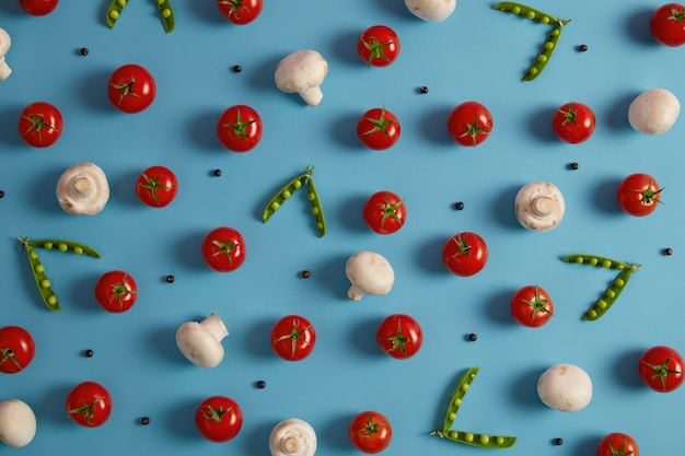 Frisches Gemüse, Zutaten zum Kochen von Suppe oder Salat. Champignons, rote Tomaten, grüne Erbsen und Pfefferkörner auf blauem Hintergrund. Gesunde Ernährung, Nährstoffe. Selektiver Fokus über der Aufnahme