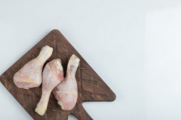 Frisches Huhn auf hölzernem Schneidebrett über weißem Hintergrund.