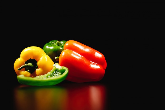 Kostenloses Foto frisches, leckeres und gesundes essen. rote, gelbe und grüne paprikas lokalisiert auf schwarzem hintergrund