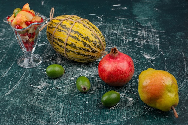 Frisches Obst und Glas geschnittener Obstsalat auf Marmoroberfläche.