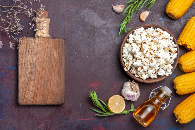 Frisches Popcorn der Draufsicht mit rohen gelben Hühneraugen auf dem dunklen Oberflächensnack-Popcornmais