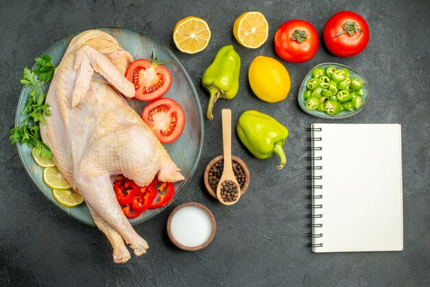 Frisches rohes Hühnchen von oben mit grüner Zitrone und Gemüse auf dunklem Hintergrund