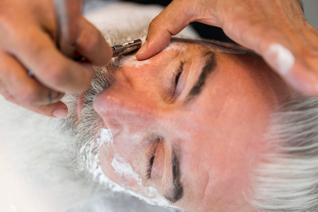 Friseur, der dem Kunden im Salon Schnurrbart rasiert