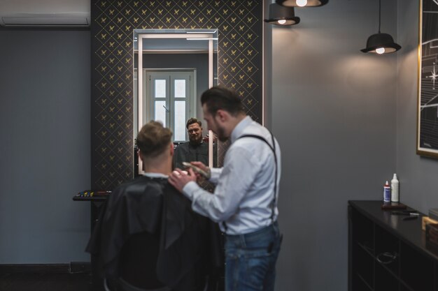 Friseur, der Haar des Kunden nahe Spiegel rasiert