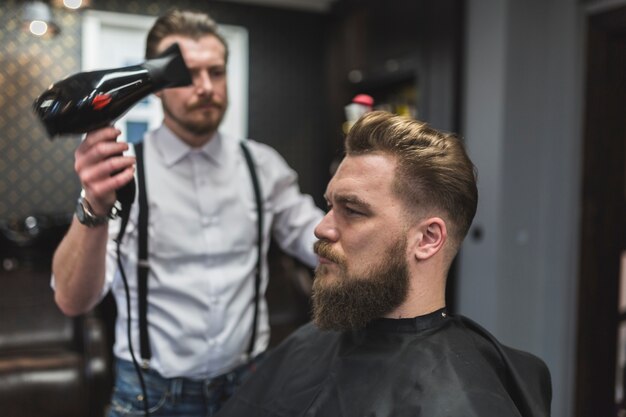 Friseur, der Trockner auf Haar des Kunden verwendet