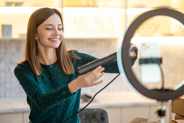 Friseur. Lächelnder junger Friseur, der Haarglätter hält und zufrieden aussieht