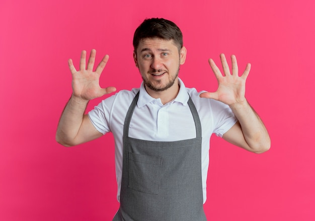 Friseur Mann in der Schürze zeigt und zeigt mit den Fingern Nummer zehn lächelnd über rosa Wand stehend