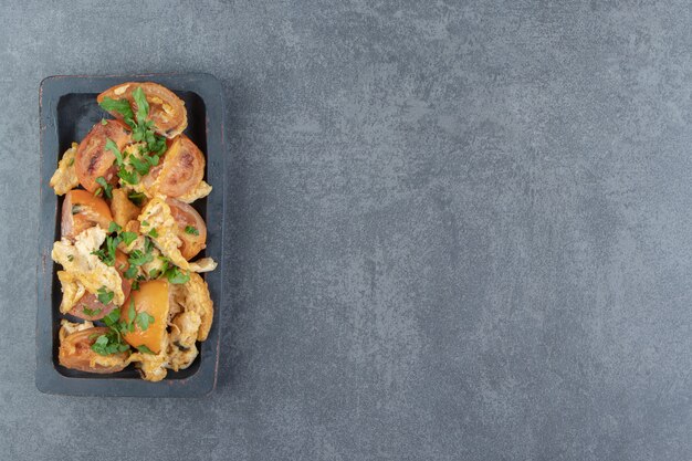 Frittierte Eier mit Tomaten auf schwarzem Teller.