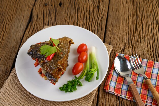 Frittierte Fischköpfe mit Chilis auf einem weißen Teller mit Tomaten und Frühlingszwiebeln.