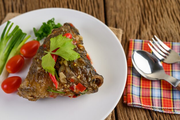 Frittierte Fischköpfe mit Chilis auf einem weißen Teller mit Tomaten und Frühlingszwiebeln.