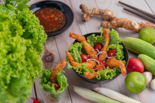 Frittierter Garnelenteig auf Salat und Tomaten in einer Holzschale.