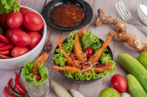 Frittierter Garnelenteig auf Salat und Tomaten in einer Holzschale.