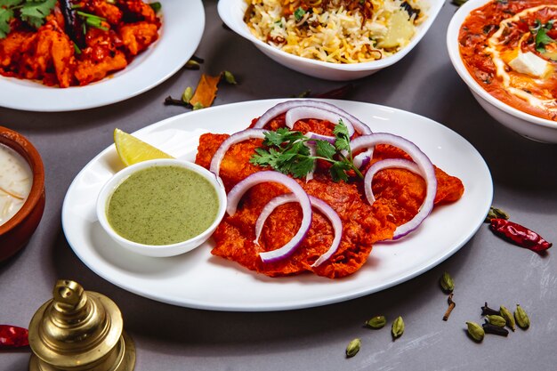 Frittiertes Fischfilet von der Seite mit roter Zwiebelsauce und Zitronenscheibe auf einem Teller