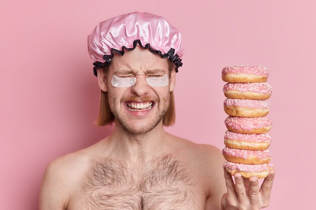 fröhlich huy mit langem haar schnurrbart trägt hydrogel flecken unter den augen hält haufen süßer leckerer donuts.