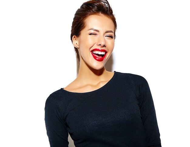 fröhlich lächelnd zwinkert Mode Frau verrückt in lässig schwarzer Kleidung mit roten Lippen auf weiße Wand