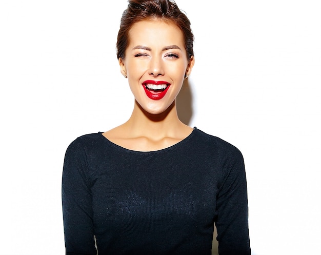 fröhlich lächelnd zwinkert Mode Frau verrückt in lässig schwarzer Kleidung mit roten Lippen auf weiße Wand