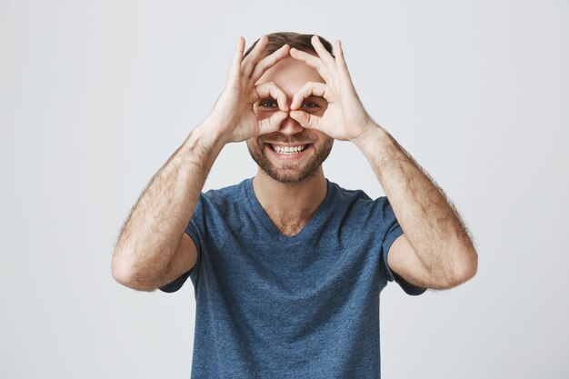 Fröhlich lächelnder gutaussehender Mann zeigen okay Zeichen über den Augen