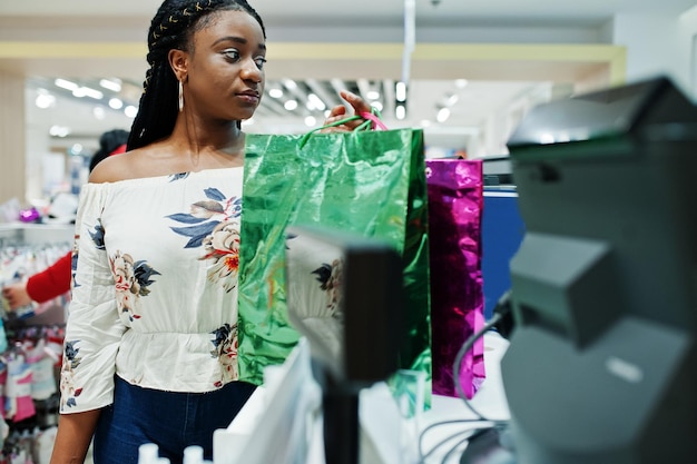Fröhliche afrikanisch-amerikanische Kundin mit farbigen Einkaufstaschen, die in der Nähe des Kassenterminals bezahlen