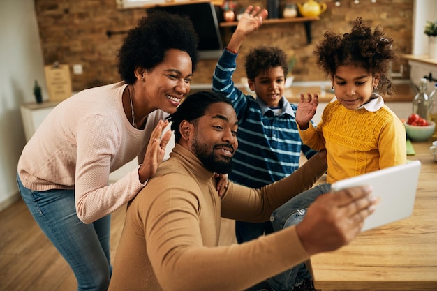 Fröhliche afroamerikanische Familie winkt während eines Videoanrufs über ein digitales Tablet zu Hause