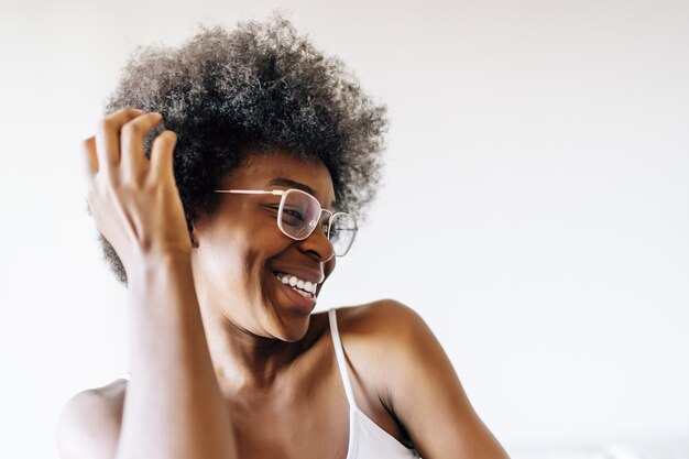 Fröhliche afroamerikanische Frau posiert gegen eine weiße Wand