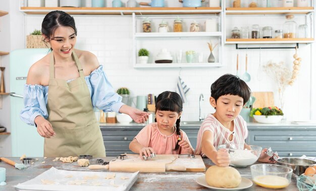 Fröhliche asiatische Familie bereitet Teig zu und backt Kekse in der Küche zu Hause Genießen Sie die Familie