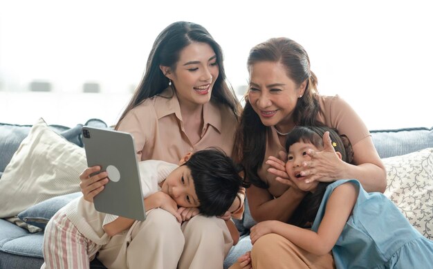 Fröhliche asiatische Familie mit Großmutter, die zu Hause gemeinsam das Tablet benutzt