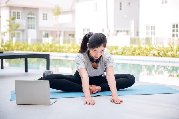 Fröhliche asiatische Frau, die morgens zu Hause im Freien Übungen und Yoga-Training ausdehnt