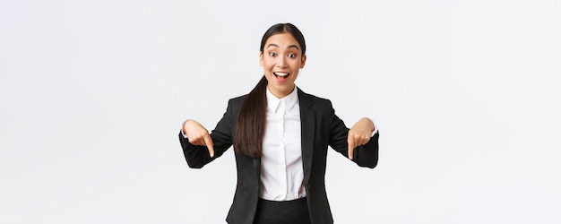 Fröhliche aufgeregte asiatische Unternehmerin im Anzug, die mit dem Finger nach unten zeigt, um das beste Preisangebot zu zeigen Formale Kleidung der Industriellen Frau mit unterer Werbung mit amüsiertem Lächeln weißem Hintergrund