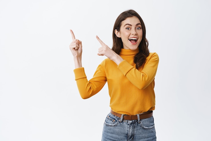 Kostenlose Foto fröhliche, aufrichtige frau, die auf das logo in der oberen linken ecke zeigt und lächelt, das werbebanner oben zeigt und gegen die weiße wand steht