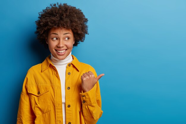 Fröhliche erwachsene Frau mit Afro-Frisur drückt aufrichtige Gefühle aus, lächelt glücklich