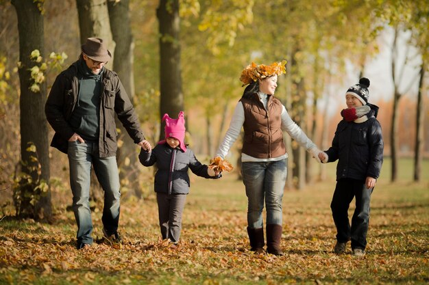 Fröhliche Familie, die Spaß beim Laub hat Eltern und ihre Kinder, die alle zusammen im Herbstwald spazieren gehen und lachen