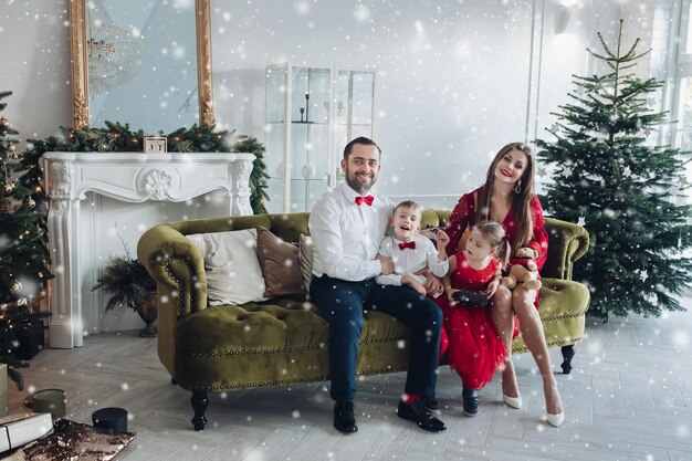 Fröhliche festliche familie, die im luxuriösen dezember-ferieninnenraum am weihnachtsbaumhintergrund lächelt