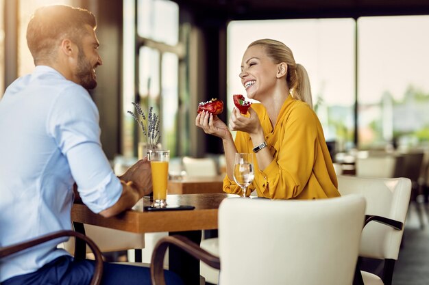 Fröhliche Frau, die Donut isst und mit ihrem Freund in einem Café spricht