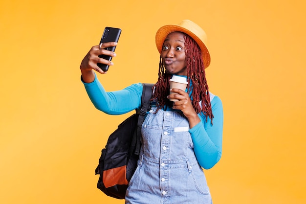 Fröhliche Frau, die im Urlaub Fotos macht und sich auf internationaler Reise im Studio mit Kaffee aufgeregt fühlt. Junge Person, die Spaß mit Bildern hat, urbanes Abenteuer mit Bildern.