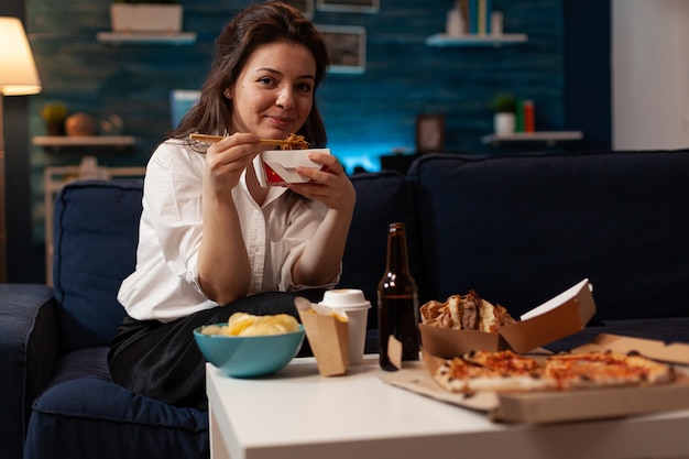 Fröhliche Frau, die leckeres chinesisches Essen isst und sich auf der Couch entspannt